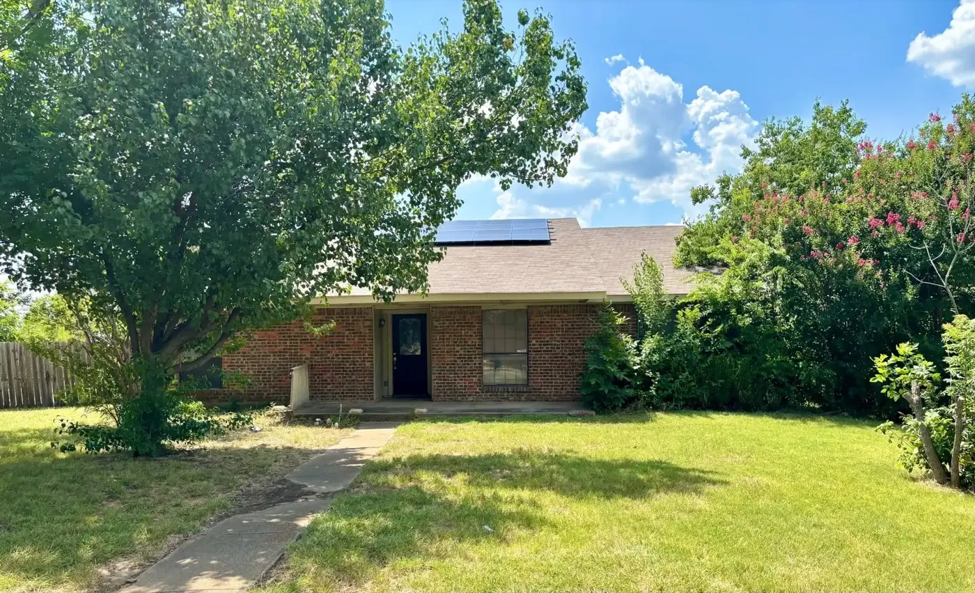 Brick house with solar panels under a large tree, bought by Tara Pays Cash